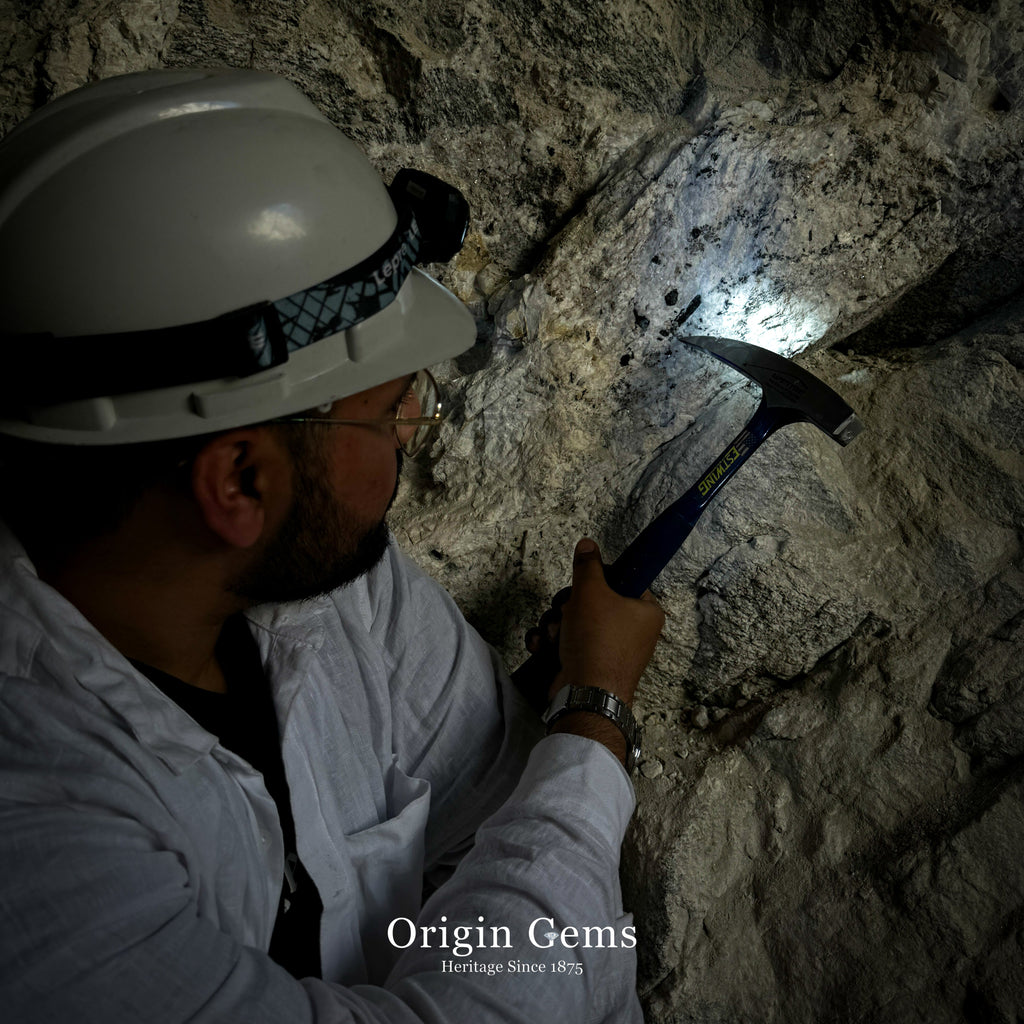 Person in a hard hat using a flashlight and hammer inside Shigar Skardu Aquamarine mine